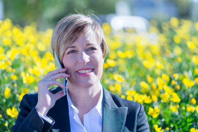 Professional woman speaking on cell phone in front of yellow flower hedge