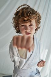 Serious boy practicing karate in room near curtain