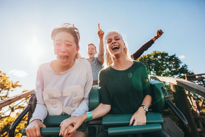 Enthusiastic young friends riding roller coaster ride at amusement park