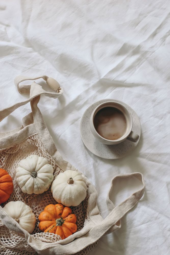 Little orange pumpkins in ecological reusable cotton mesh bag, cup of coffee, linen fabric table background