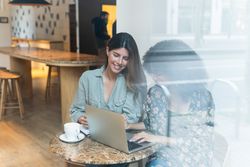 Smiling multiracial girlfriends sharing laptop in coffee shop