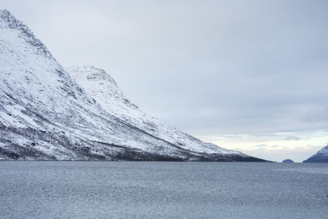 Tranquil lake against snowy hills in cold overcast weather