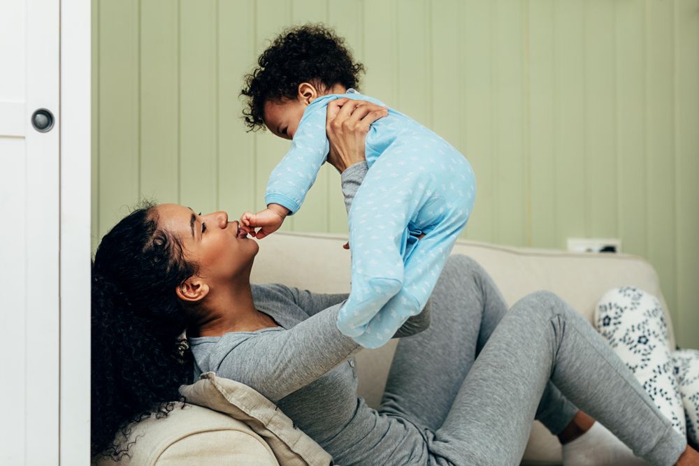 Mother lying on sofa holding her toddler boy above her