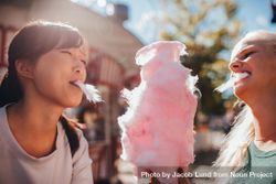 Two young women sharing cotton candy at amusement park 4OjLg5