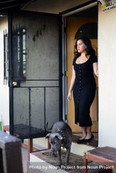 Beautiful woman standing at front door looking out with her dog nearby 4MGda0