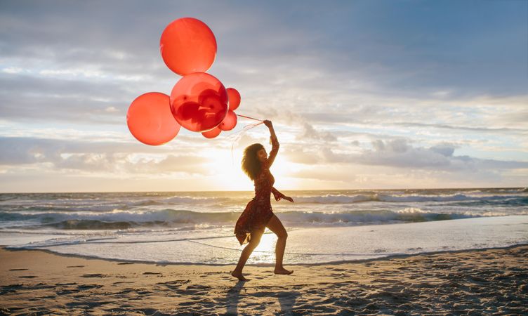 Beautiful woman holding bouquet of balloons at the beach
