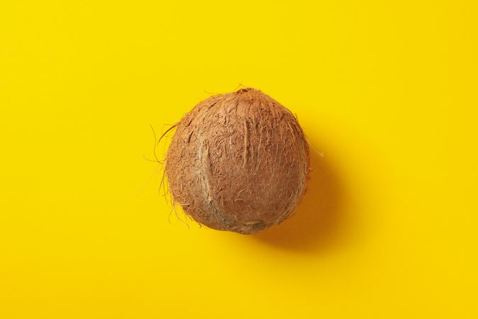 Whole coconut on yellow background, top view