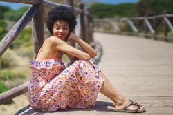 Smiling woman in maxi dress sitting on footbridge in the sun