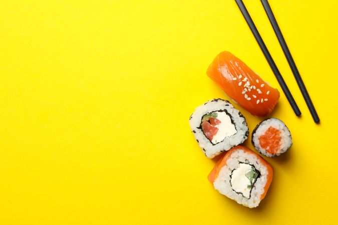 Chopsticks and sushi rolls on yellow background, space for text. Japanese food