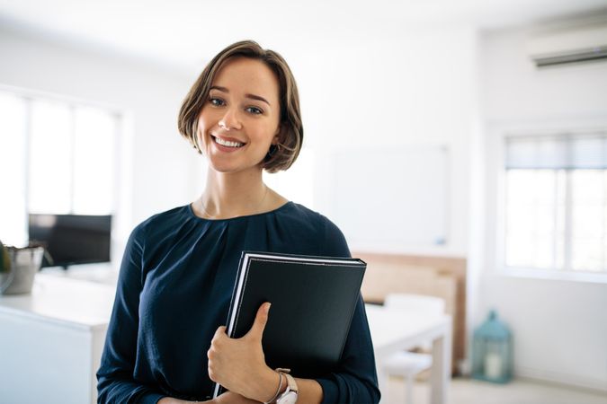 Smiling businesswoman standing in office holding a diary