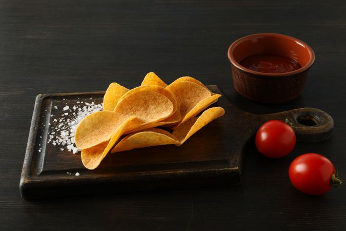Potato chips on a wooden board with salt on a dark background