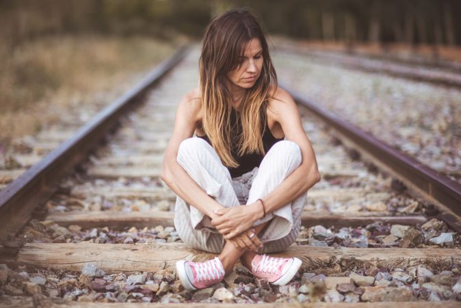 Long haired woman sitting on railways overgrown with dry grass