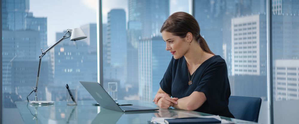 Portrait of Successful Young Businesswoman Sitting at Her Desk Working on Laptop in Big City Office.
