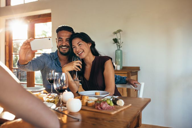 Cheerful couple taking selfie while having dinner with friends at home