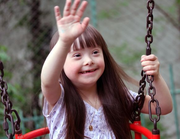 Young girl with Down syndrome waving from a swing