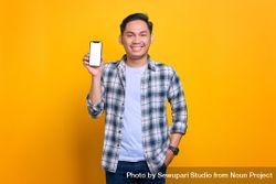 Smiling Asian male with hand in pocket and showing blank screen of smart phone 56m1P0