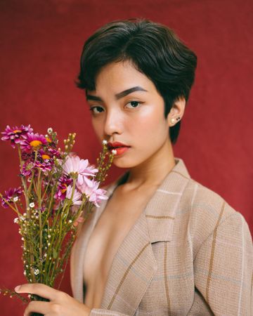 Woman in beige blazer holding purple flowers against red background