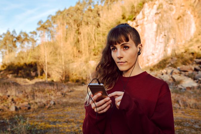 Young woman with piercing listening music on smartphone on hill