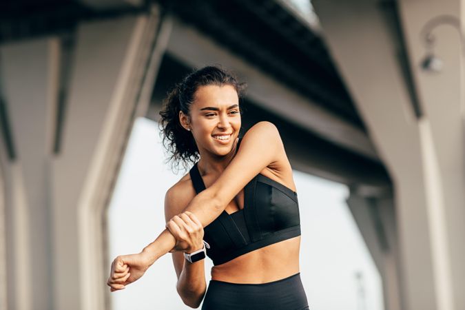 Smiling female stretching arm outdoors