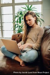 Young woman sitting on her couch working on laptop 0LLYr0
