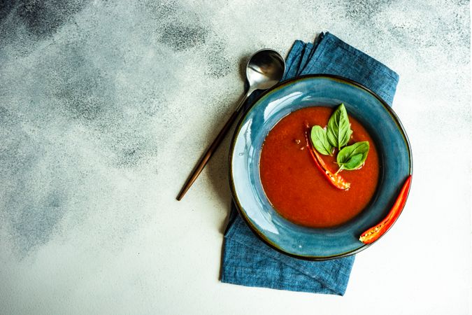 Top view of traditional Spanish soup of tomato gazpacho with basil garnish in blue bowl and copy space