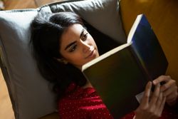 Female lying on pillows reading a green book