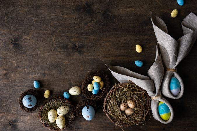Easter eggs wrapped with rabbit ears with napkin with bird nests on wooden table