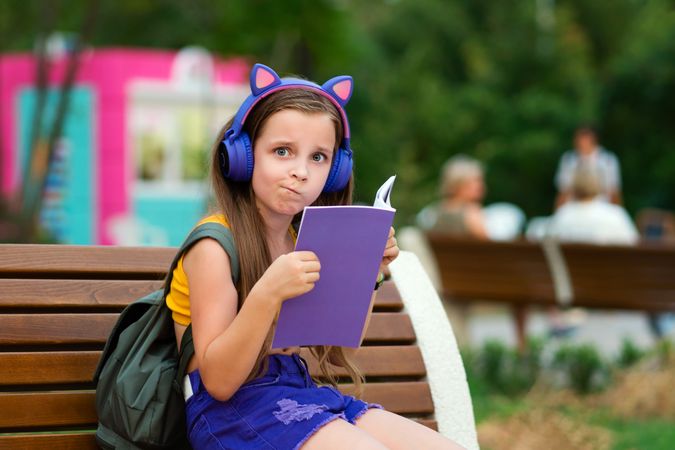 Preteen school girl with book on bench in park