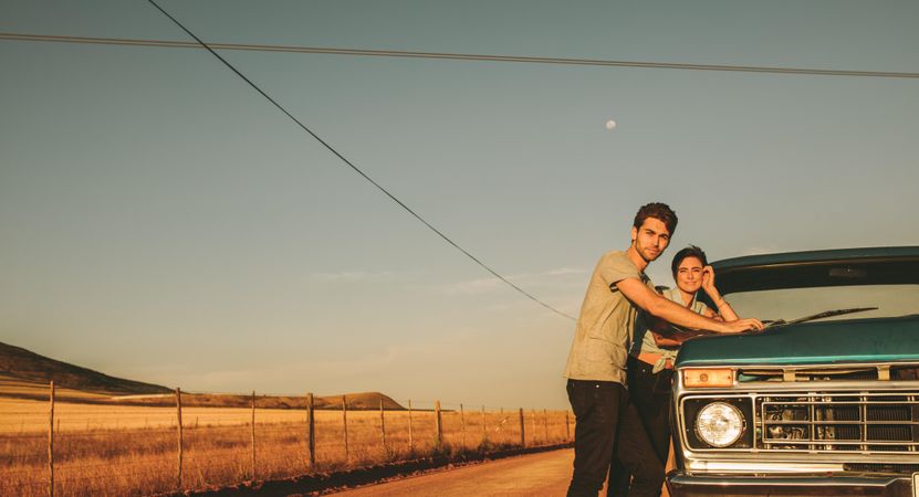 Young man and woman leaning on classic truck looking at sunset