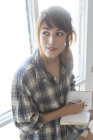 Female in flannel shirt journaling and daydreaming while leaning on window