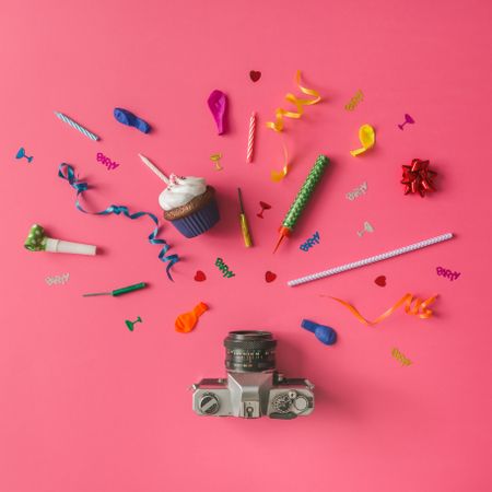 Camera with colorful party items on pink background