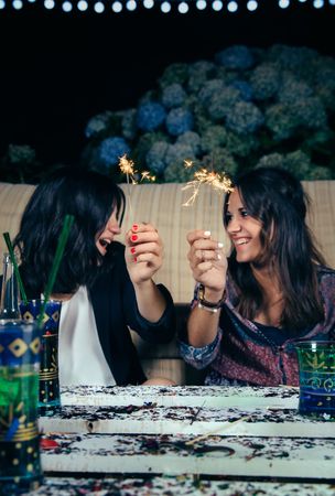Happy female couple holding sparklers at a party