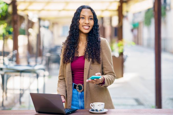 A confident young woman is diligently working on her laptop at a cozy outdoor cafe setting,
