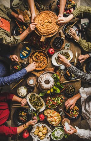 Group of people at wooden table with meze feast, reaching for flat bread