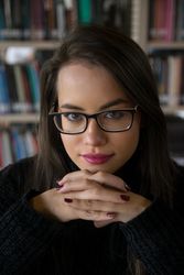 Woman sitting along bookshelves and looking at camera