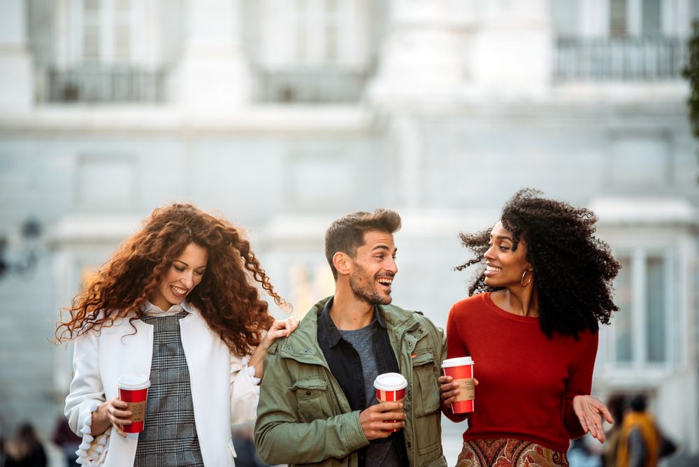 Three young friends walking and drinking coffee