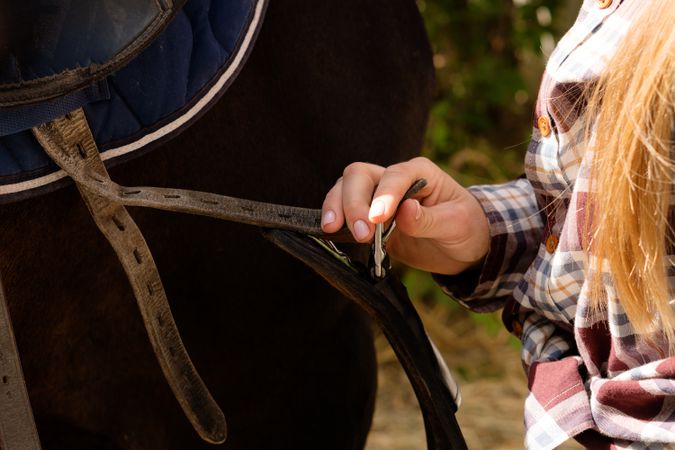 Equestrian adjusting saddle on horse.