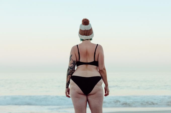 Rearview of unrecognizable woman looking at the sea water in winter wearing a bikini and hat