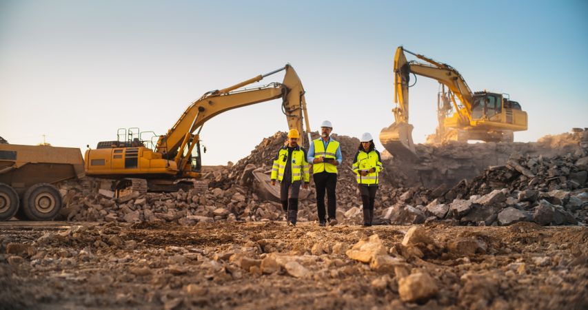 Construction Site With Excavators on Sunny Day: Diverse Team Of Male And Female Specialists Walking And Discussing Real Estate Project. Civil Engineer, Architect, Urban Planner Talking, Using Tablet.