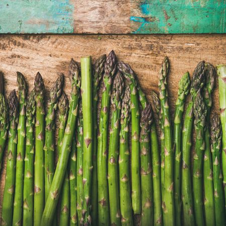 Asparagus lined up on wooden board with green trim, square crop with copy space