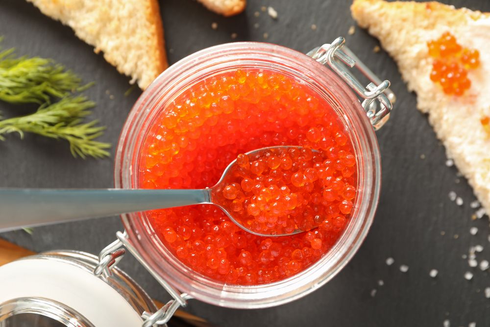 Composition with caviar in glass jar, bread, spoon and cutting board, top view