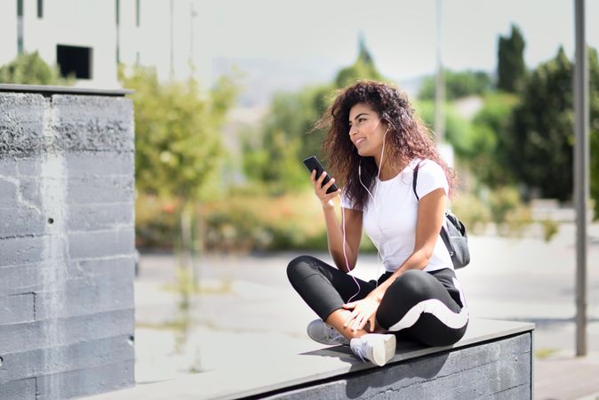 Arab woman talking on phone through headphones sitting outdoors