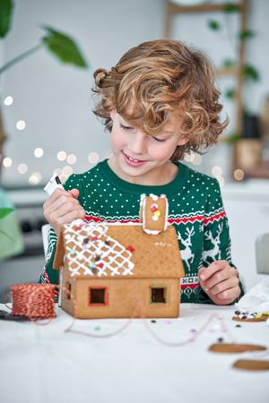 Content boy applying icing on sweet gingerbread house