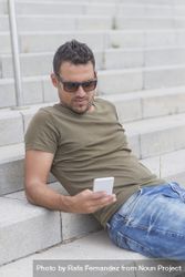 Man sitting on outdoor stairs while texting on phone, vertical 0yZn15