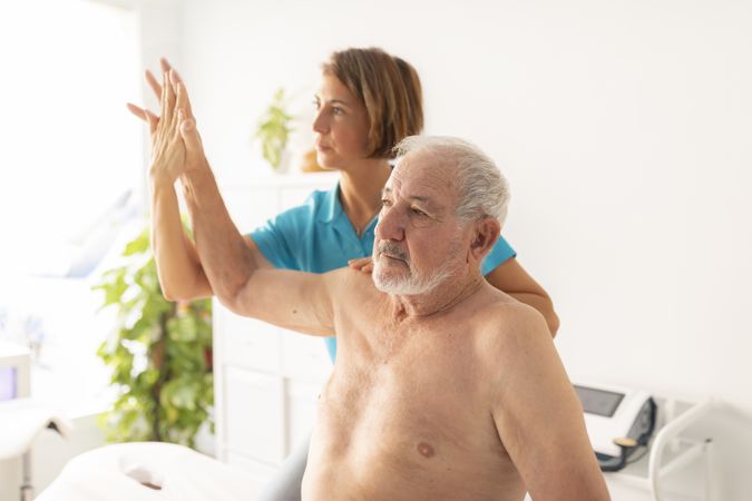 A female physiotherapist performs a massage and checks the mobility of the arm and shoulder of her mature male patient