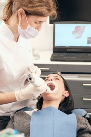 Focused doctor examining teeth of client with 3D scanner