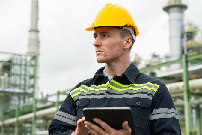 Refinery oil engineer worker in protection hardhat with digital tablet inspecting at petrochemical factory.