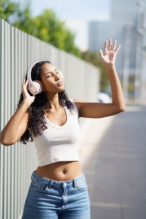 A joyful and happy young woman is enjoying music outdoors while wearing stylish headphones