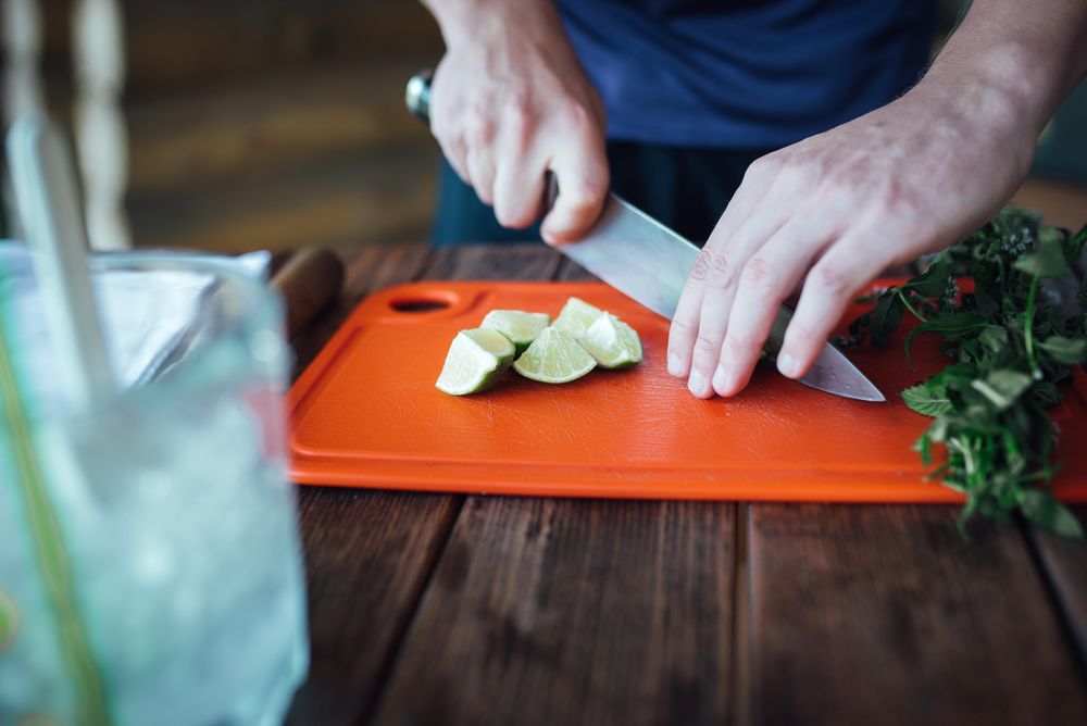 Person slicing lime on red chopping board