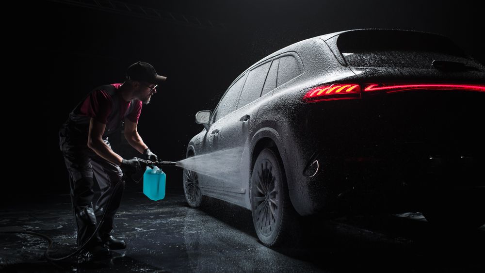Professional Car Wash Specialist Spraying Smart Foam to Prepare a Modern Electric SUV with Contemporary Design for Sale at a Dealership Car Center.